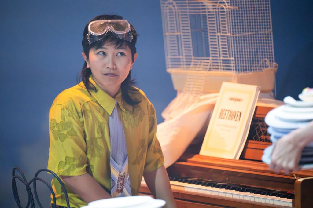 A performer in goggles at the piano in The Fall Show